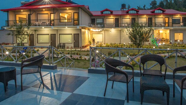 Ein Hotel mit rotem Dach, mehreren Balkonen, Außenplätzen und einem gut beleuchteten Garten.