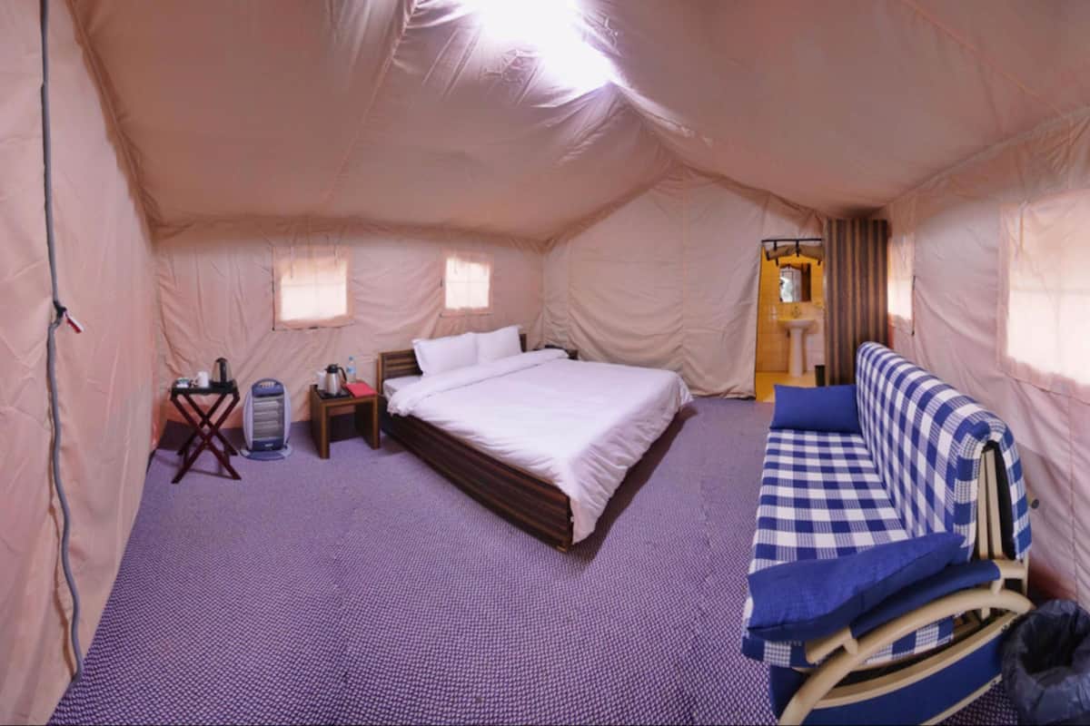 Een tentkamer met een bed, een sofa, een klein tafeltje met een waterkoker, en een raam.