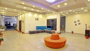 Eine großzügige Lobby mit einer modernen Sitzgelegenheit in Orange, einem großen Fenster und einer Decke mit eingelassener Beleuchtung.