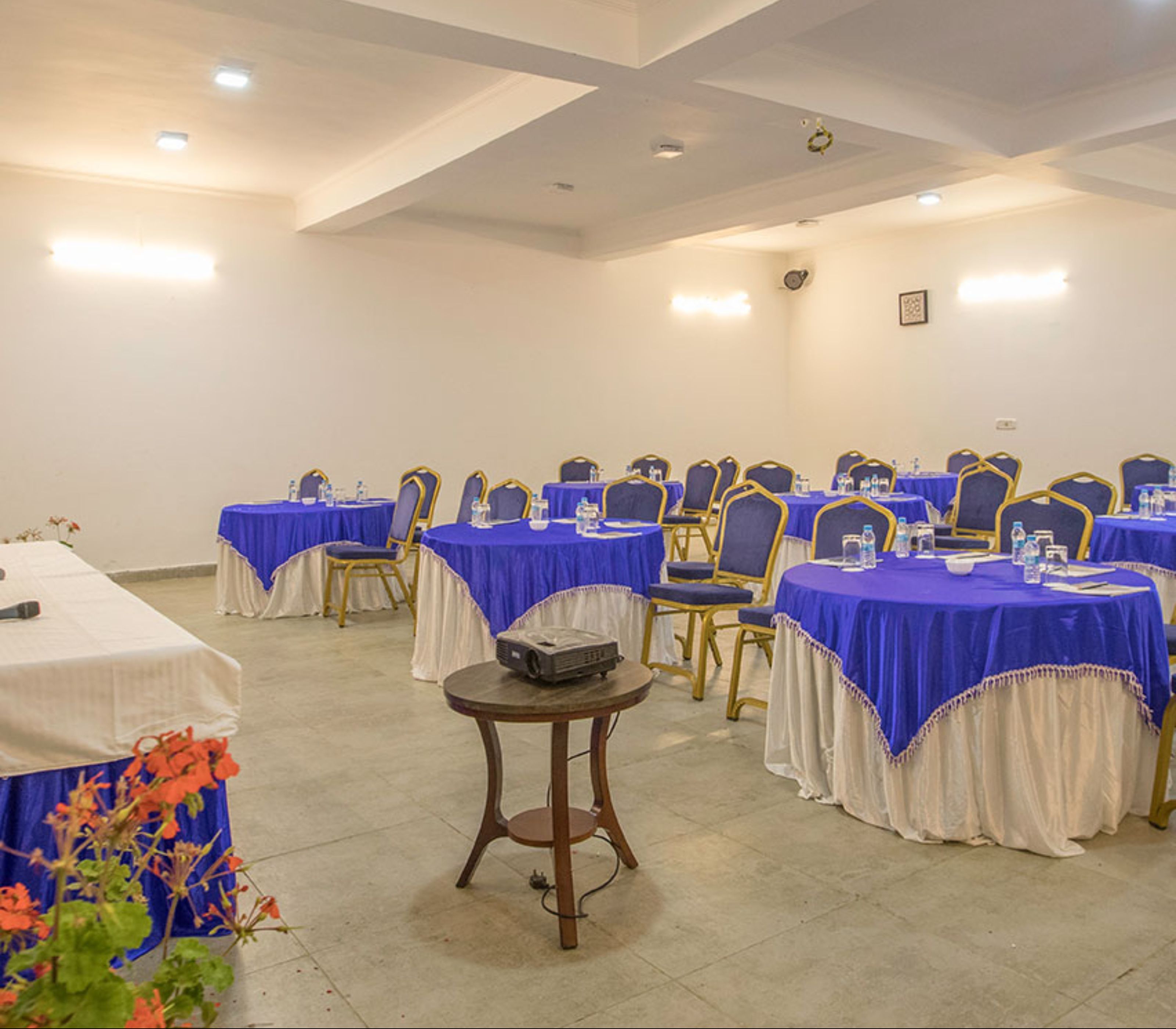 A conference room with multiple tables and chairs, equipped with water bottles and a projector.