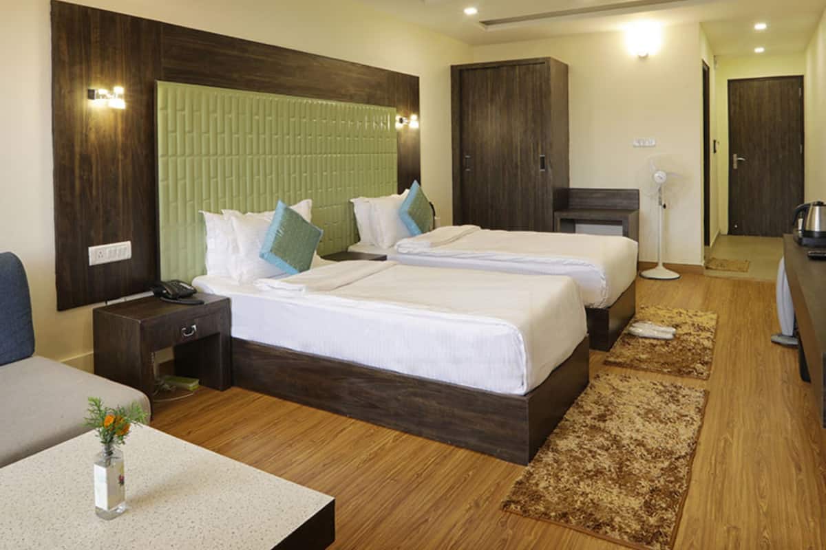 Hotelkamer met twee bedden, een bureau, een stoel, een nachtkastje, een lamp, een ventilator en een kledingkast.