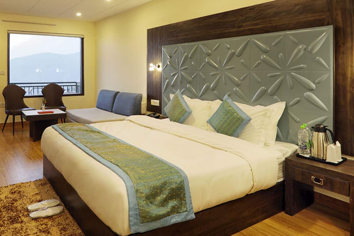 Hotelkamer met een groot bed, een bureau, een stoel, een nachtkastje met een lamp en uitzicht op de bergen door het raam.