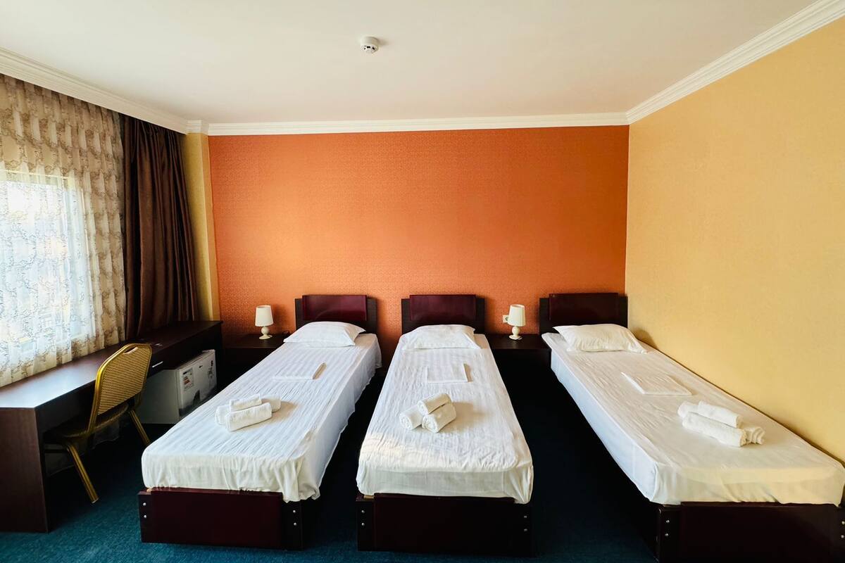 A hotel room with three single beds, a desk, and a chair.