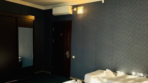Et hotelværelse med to senge, mørk væg, et spejl og en aircondition.