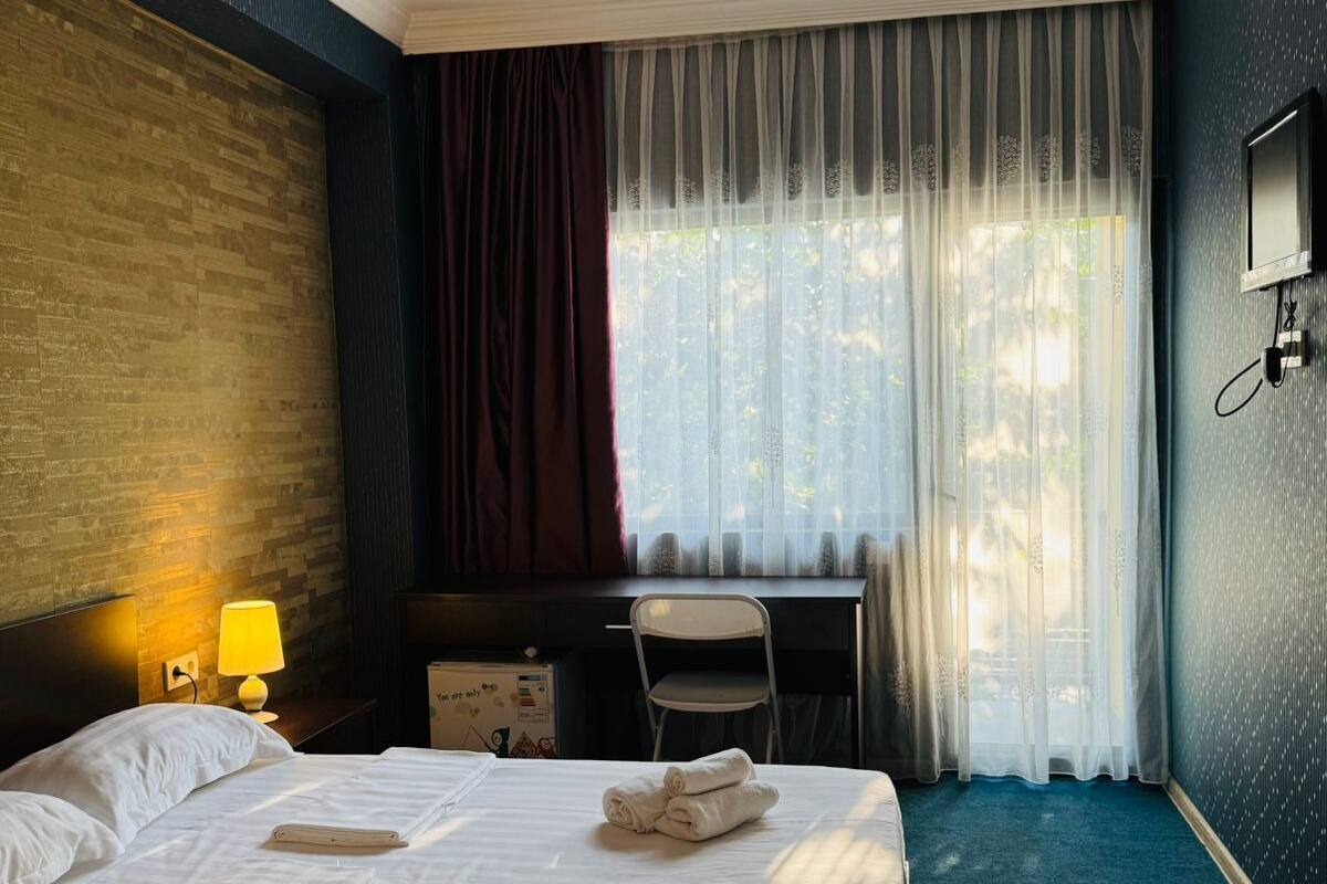 A hotel room with a large bed, a desk, a chair, a TV, and a window with curtains.