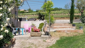 Un patio con mobiliario exterior, un pequeño jardín y vistas a un viñedo.