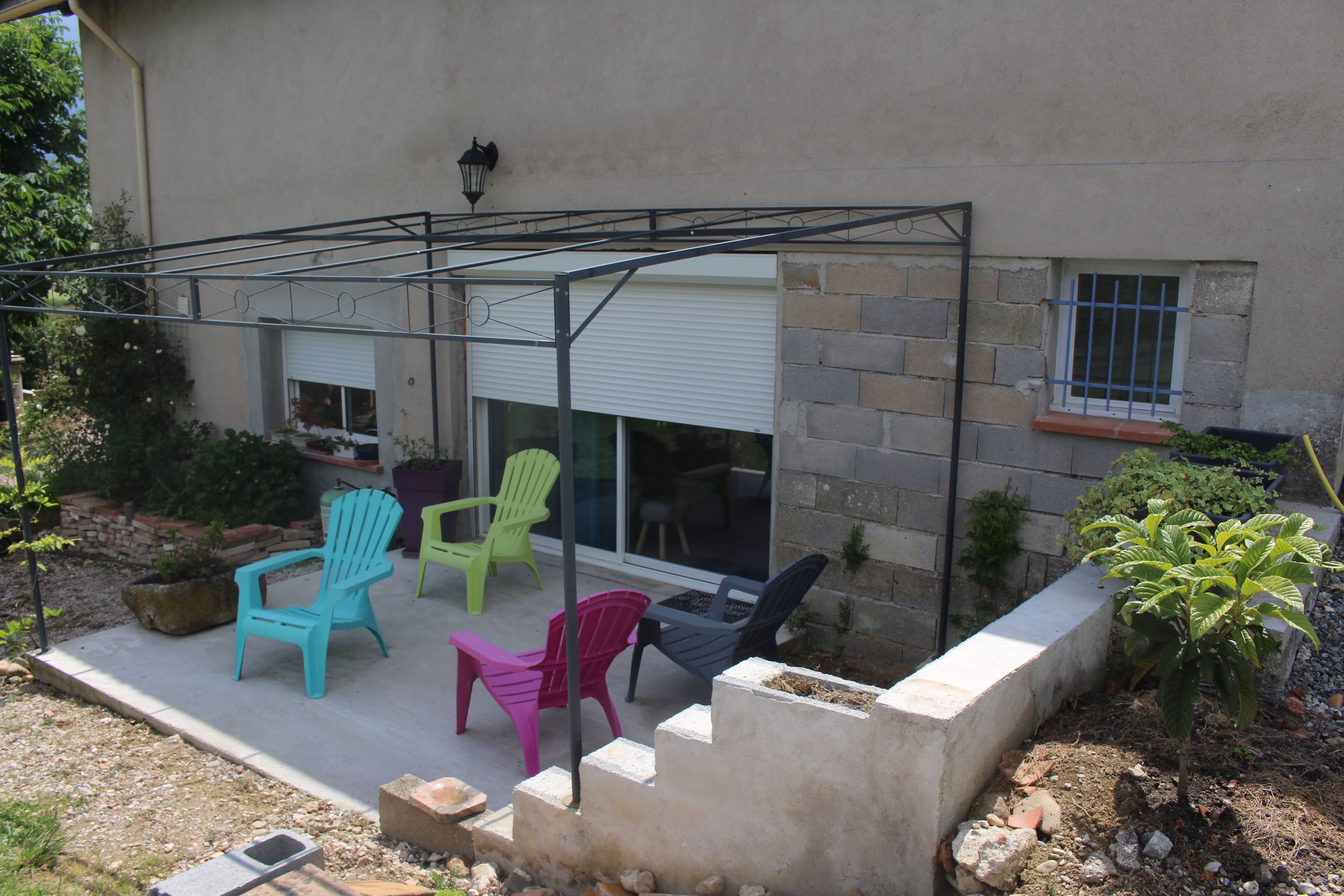 Une terrasse agrémentée de chaises Adirondack aux couleurs vives, d’un bac à fleurs en béton et d’un petit arbre.
