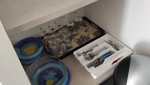 Una encimera de cocina con una cafetera, un cubo de basura y un espacio de almacenamiento con platos y cristalería.
