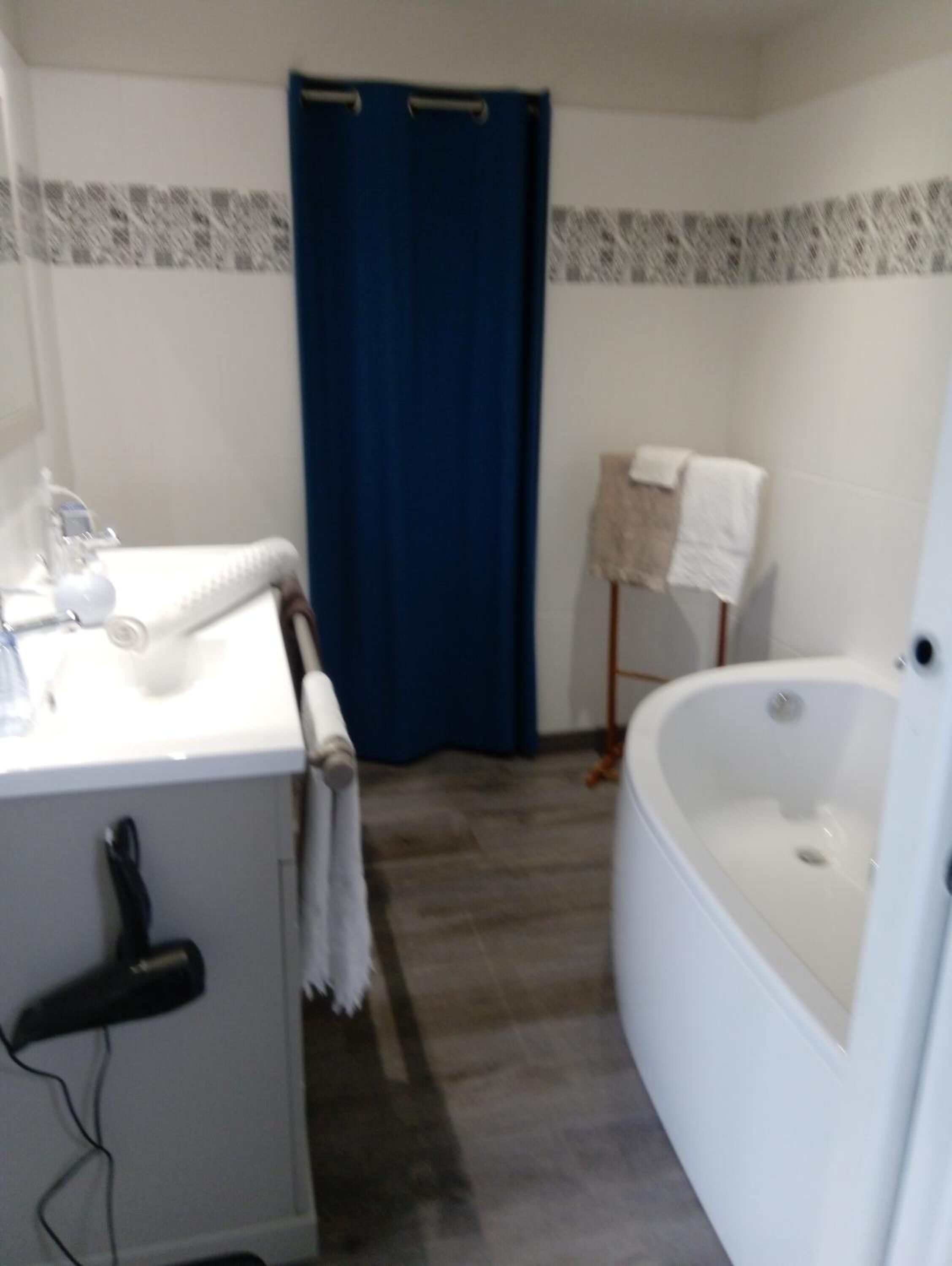 Une salle de bain avec un lavabo blanc, un sèche-cheveux, un rideau de douche bleu, un porte-serviettes et une baignoire.