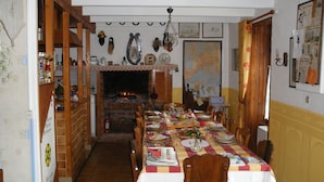 Comedor con una mesa larga dispuesta para varias personas, chimenea y varias decoraciones en la pared, incluyendo un mapa y una cabeza de caballo.