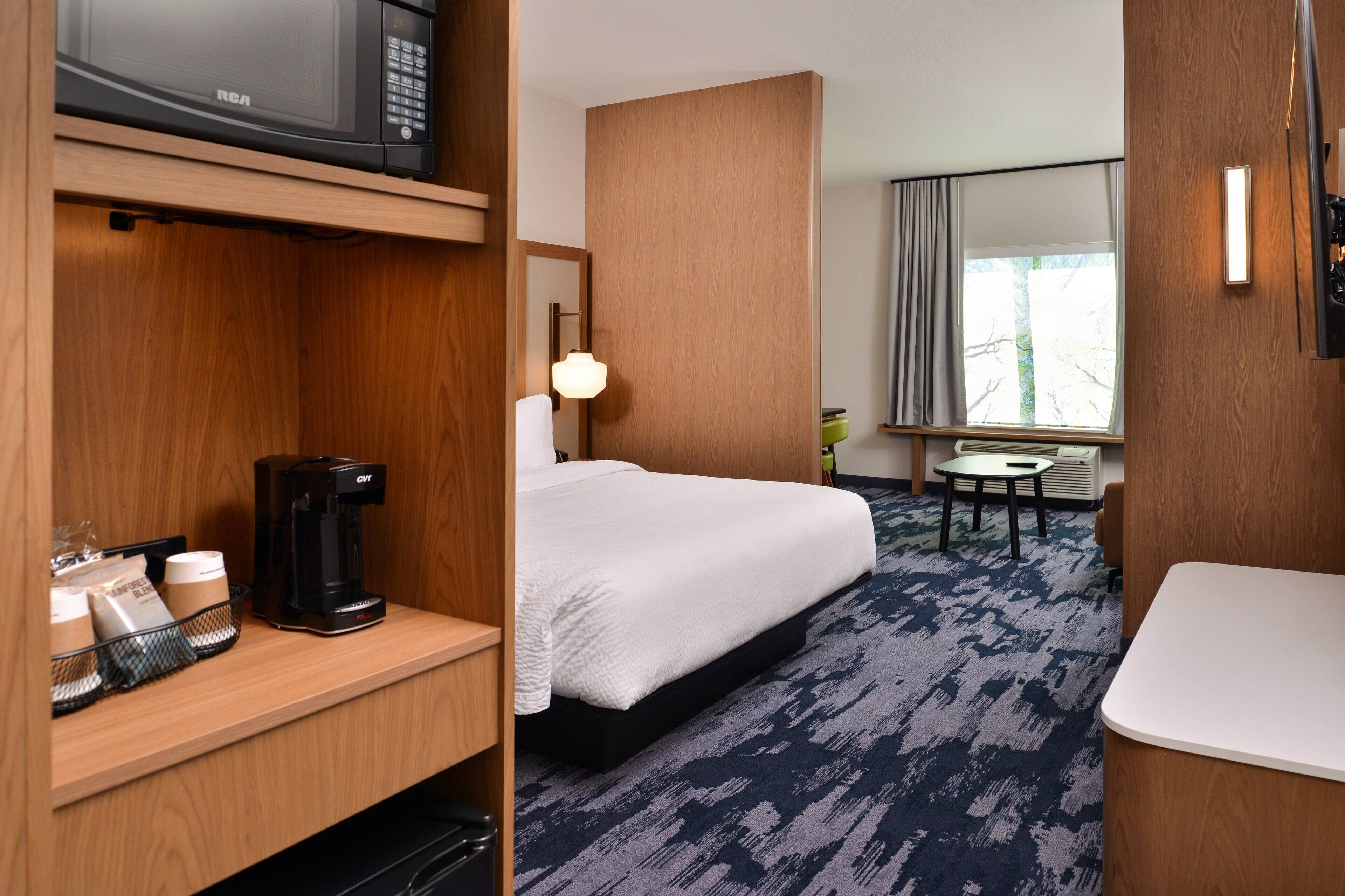 Habitación de hotel con cama, cafetera, televisión y escritorio con silla.