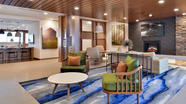 Eine moderne Lobby mit Holzboden, einer Steinsäule, einem Flachbildfernseher, einem Kamin und einem großen Teppich in Blau und Weiß.