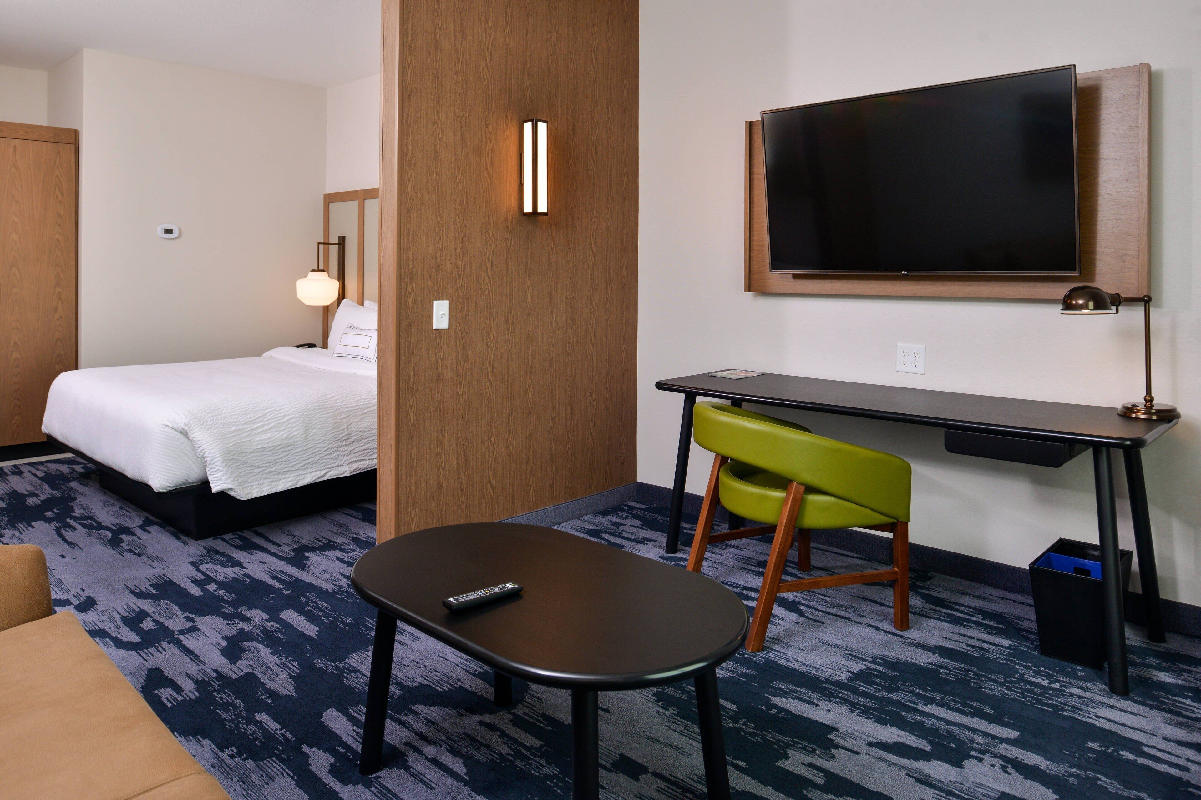 A hotel room with a bed, a desk with a chair, a television, and a remote control on the table.