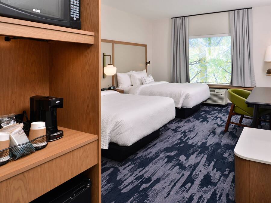 Une chambre d’hôtel avec deux lits, un bureau, une chaise, une télévision, une machine à café et une fenêtre avec des rideaux.