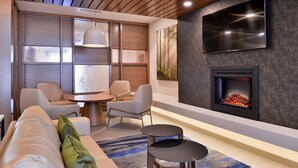 Ein modernes Wohnzimmer mit einer Couch, Sesseln, einem runden Tisch, einem Kamin und einem an der Wand befestigten Fernseher.