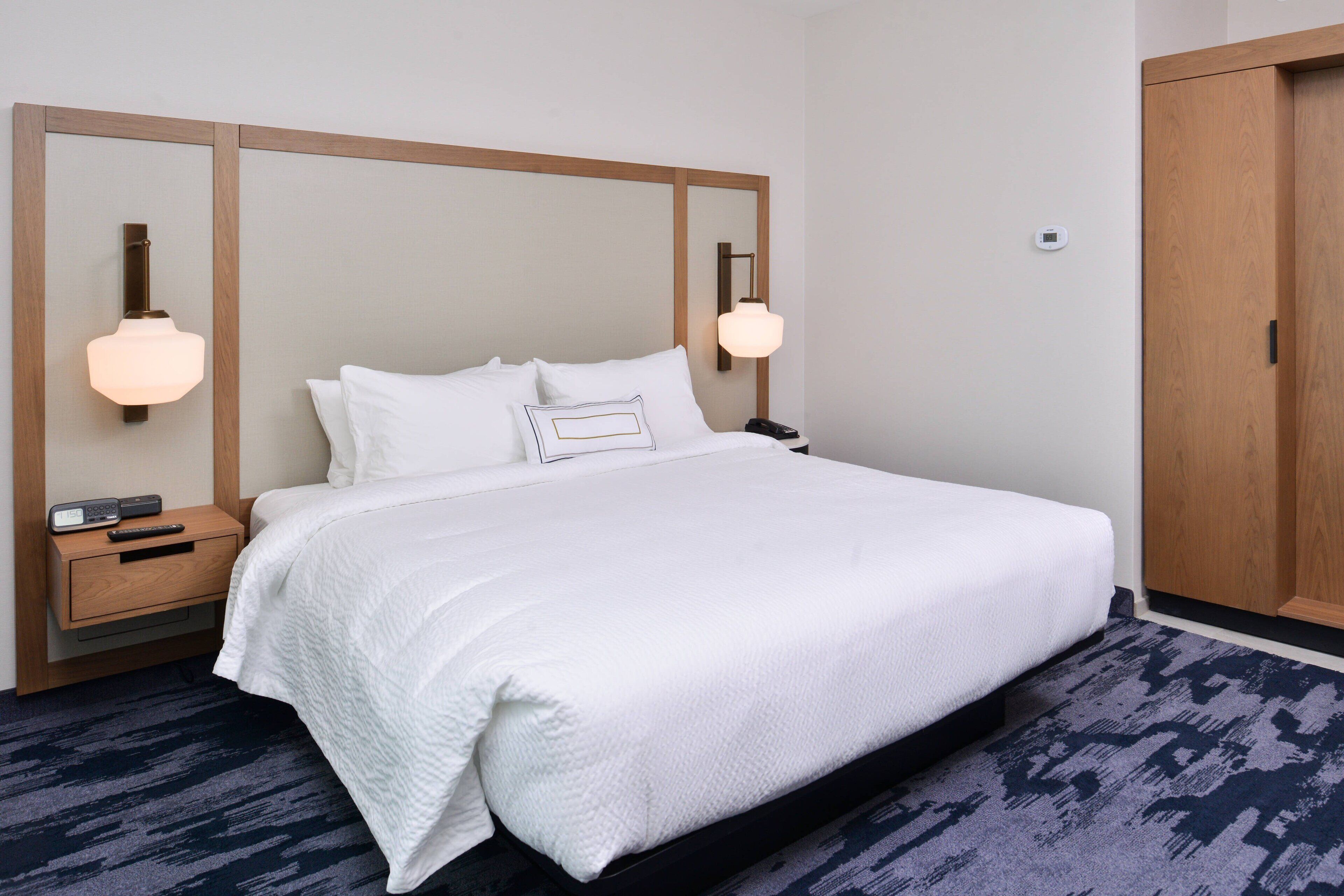 A hotel room with a large bed, wooden headboard, bedside tables with lamps, and a wardrobe.