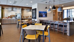 Ein modernes Restaurant mit Holzboden, gelben und grauen Stühlen sowie einer Bar mit Hockern.