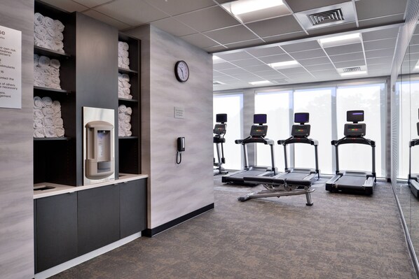 Un gimnasio moderno con dispensador de agua, un reloj y cintas de correr.