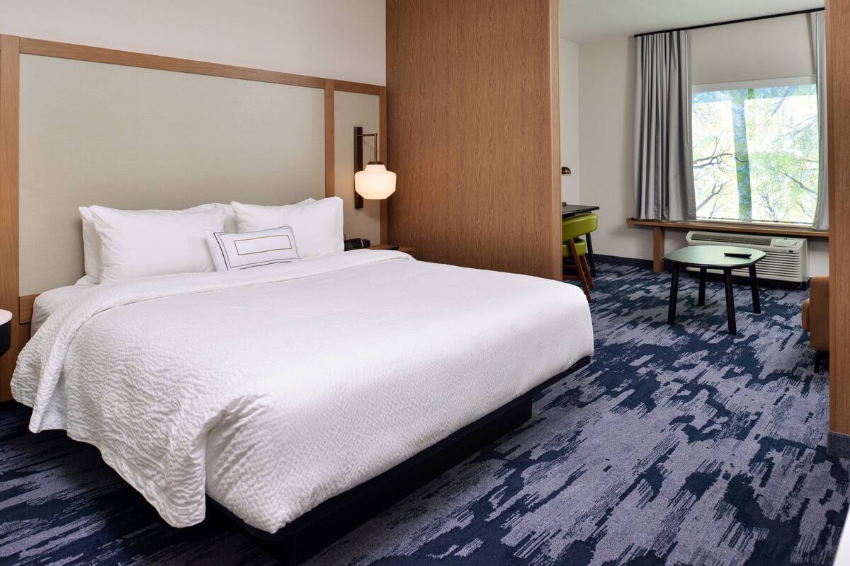 Ein Hotelzimmer mit einem großen Bett, einem Schreibtisch und Blick auf Bäume aus dem Fenster.