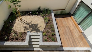 Un espace extérieur moderne doté d’une terrasse en bois, d’un jardin en briques agrémenté de plantes et d’un petit escalier menant à un niveau supérieur.