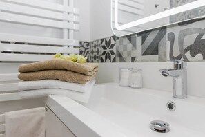 A modern bathroom with a white sink, a mirror, and a towel rack with folded towels.