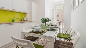 Une cuisine moderne avec des meubles blancs, un plan de travail vert et un coin repas comprenant des chaises blanches et une table dressée pour quatre personnes.