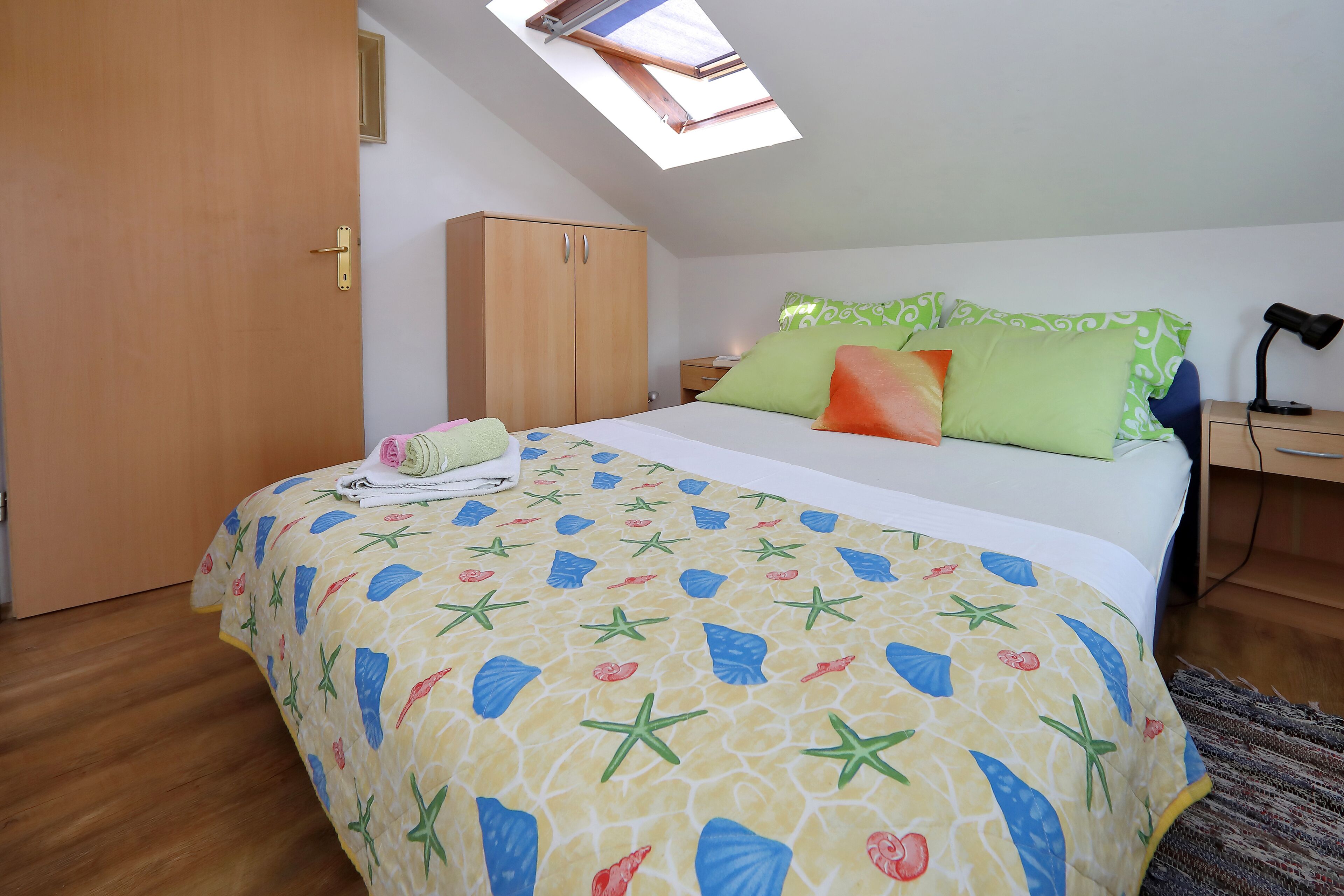 A bedroom with a bed, a wardrobe, a nightstand, and a skylight.