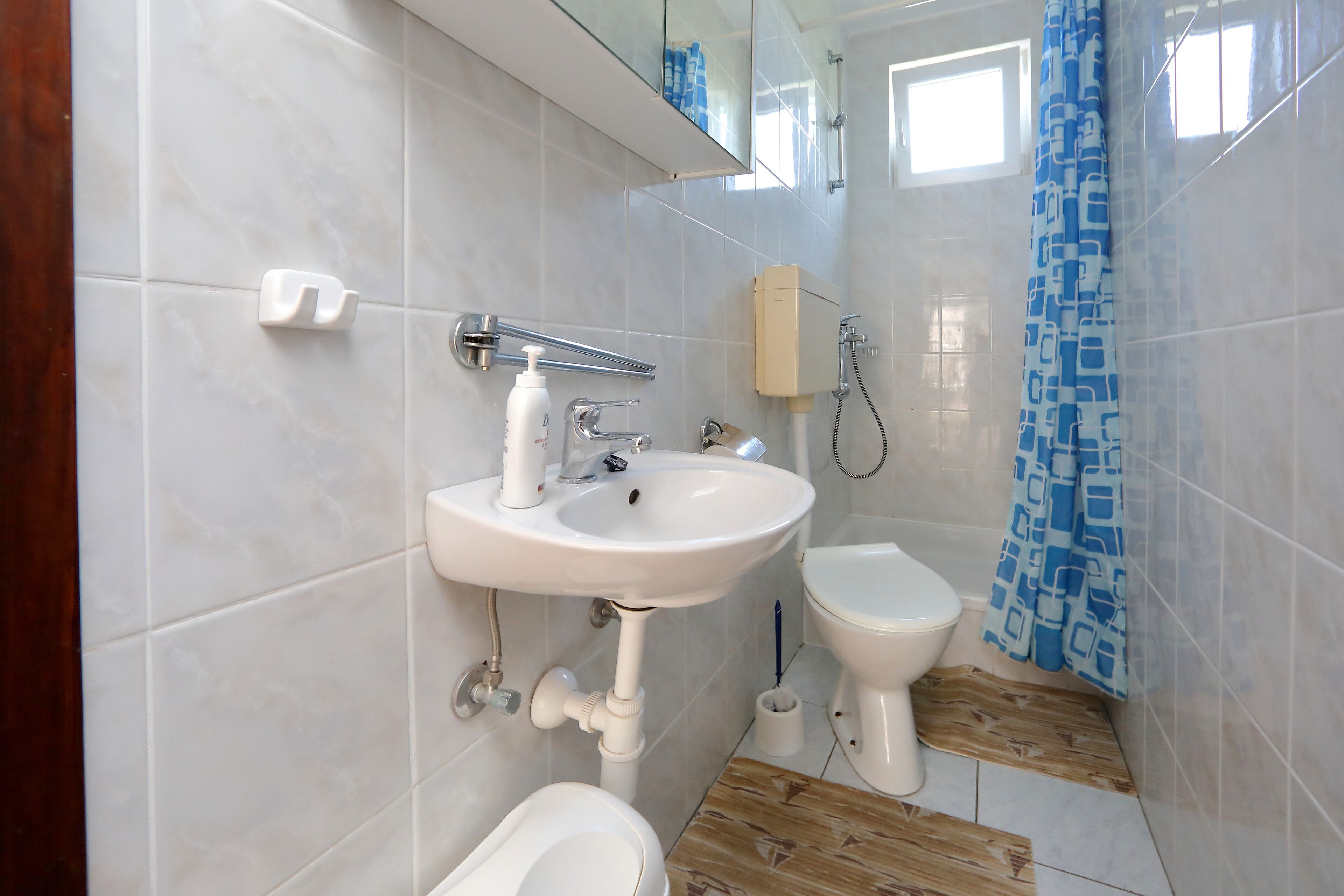 A bathroom with a white sink, toilet, and bidet, tiled walls, and a wooden floor.