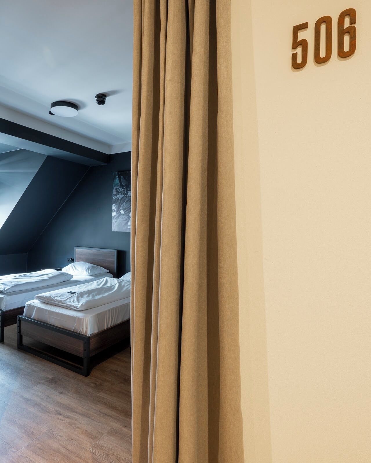 Un dormitorio moderno con dos camas, techo inclinado y el número '506' en la pared.