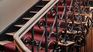 Una escalera con barandillas de hierro negro ornamentadas y peldaños alfombrados de rojo.