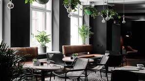 Un café moderno con decoración en blanco y negro, con plantas colgantes, asientos de cuero y un rug con estampado.