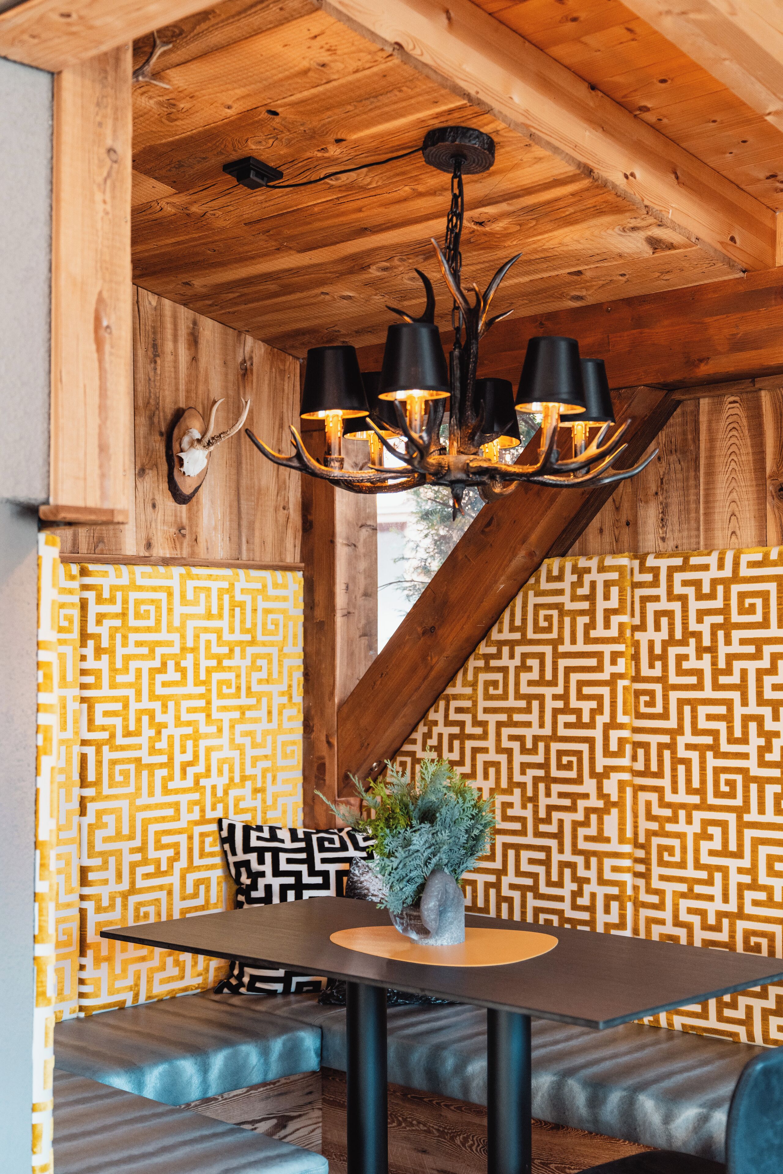 A wooden ceiling with a chandelier, a patterned wall, and a table with a plant.