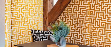 A wooden ceiling with a chandelier, a patterned wall, and a table with a plant.