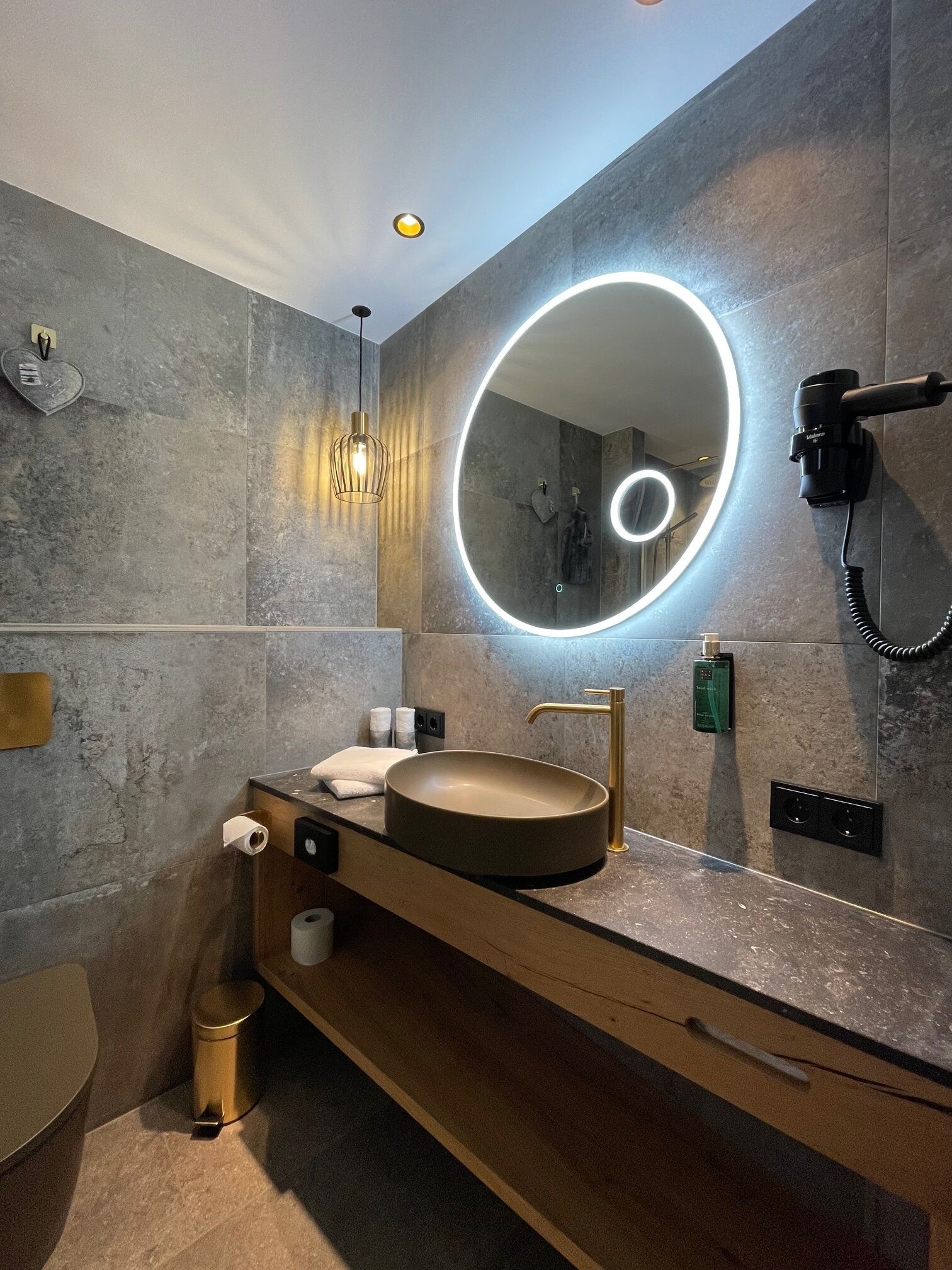 A modern bathroom with a round mirror, a sink, and a hairdryer mounted on the wall.