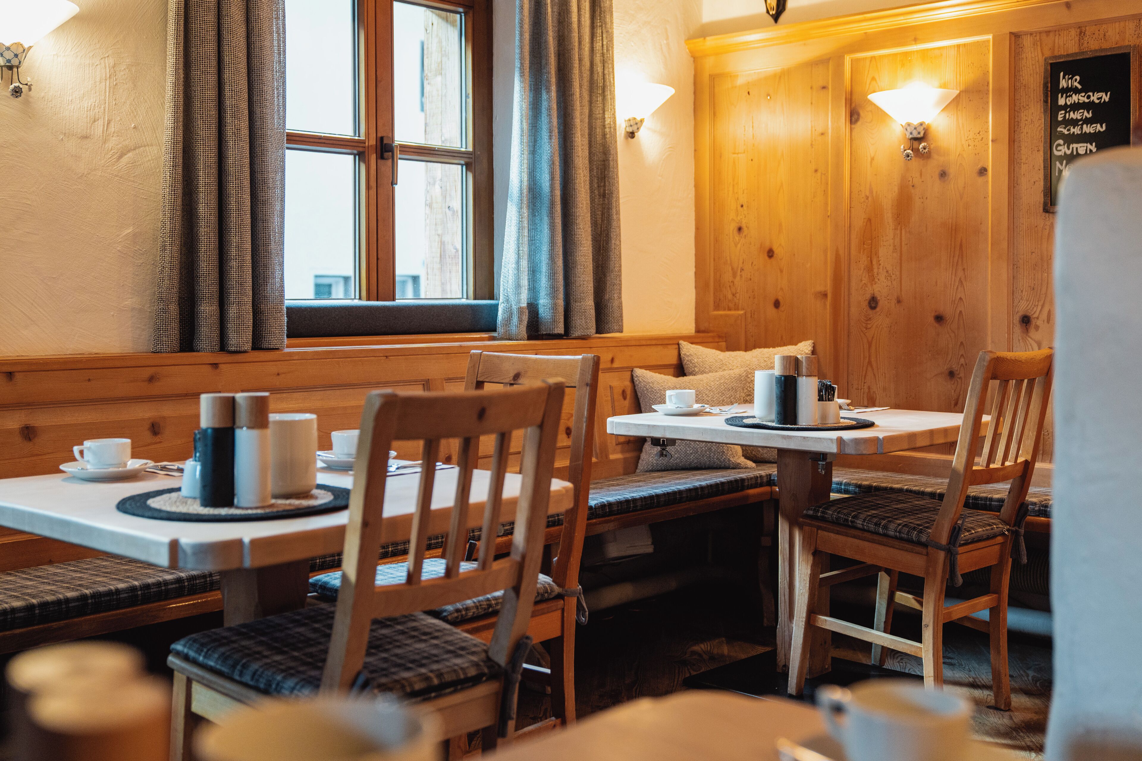 A cozy restaurant with wooden furniture, a window with curtains, and a chalkboard menu on the wall.