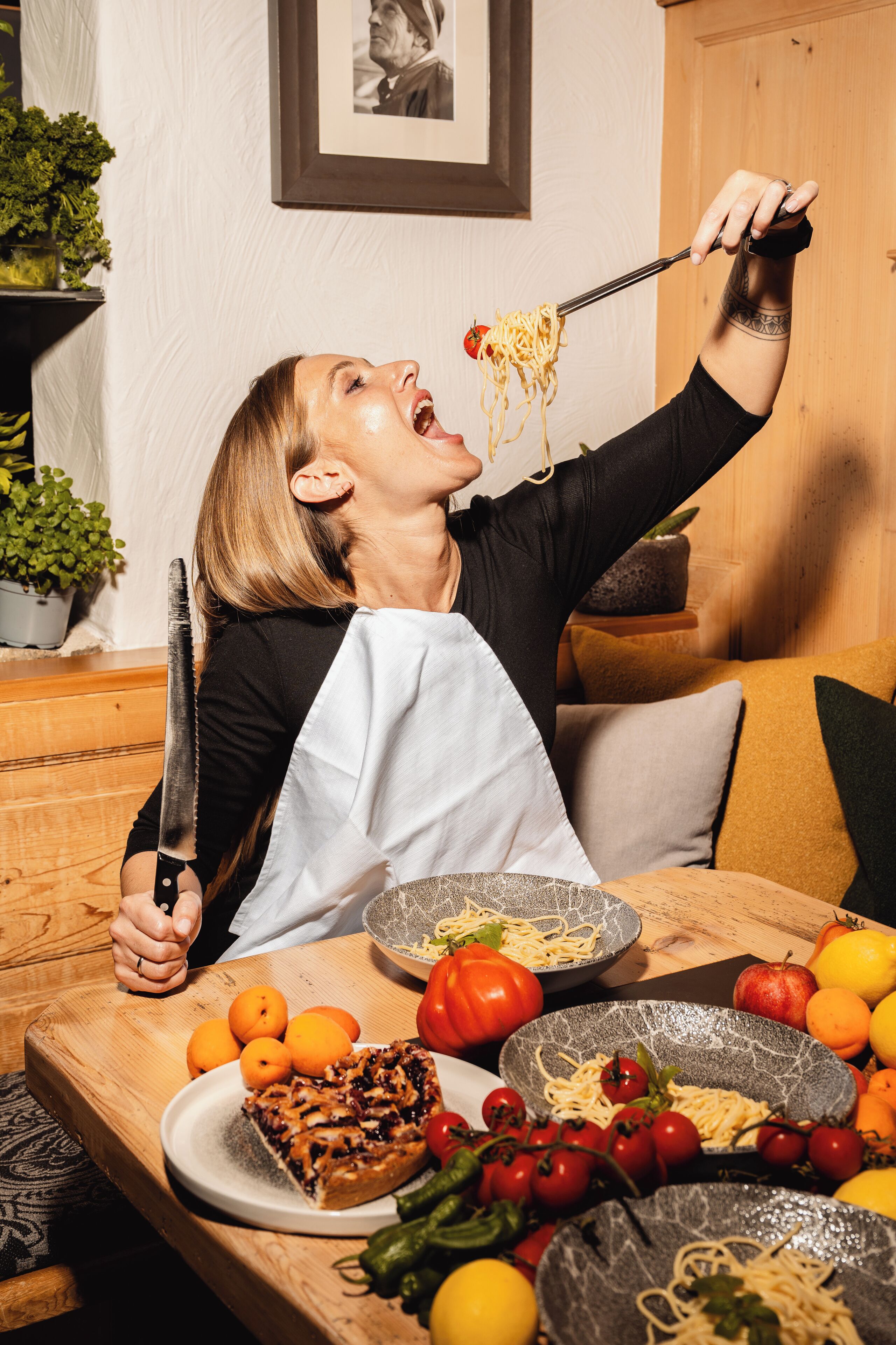 Una persona sentada en una mesa de madera con un plato de comida, un cuchillo y diversas frutas y verduras.