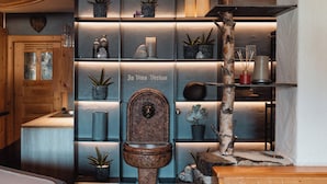Uma casa de banho com porta de madeira, uma prateleira com plantas em vasos e uma sanita fixada à parede.