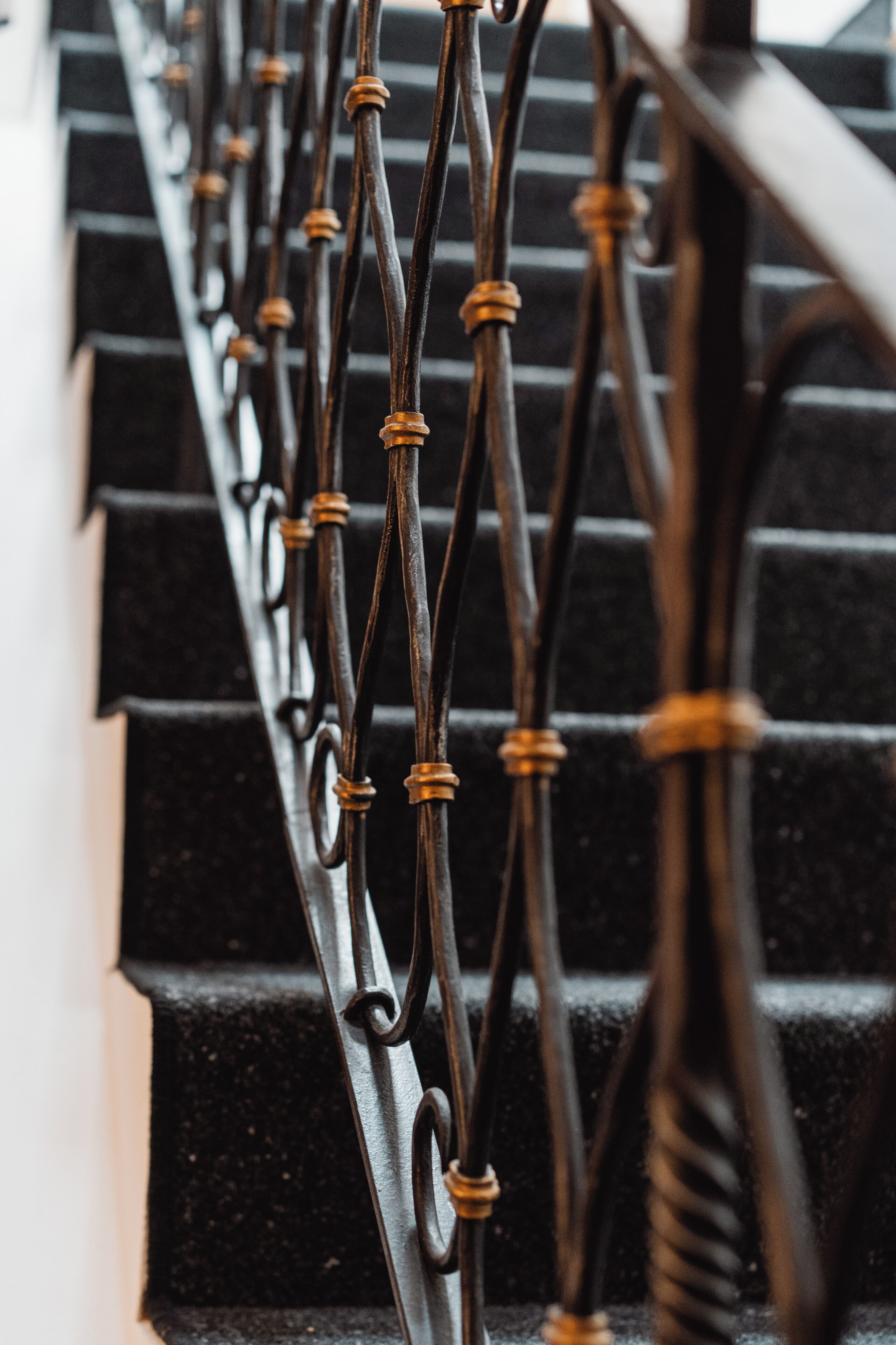 Primer plano de una escalera de metal negro con barandales ornamentados y un pasamanos.