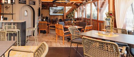 A cozy restaurant with wooden interiors, wicker chairs, and a bar area with wine bottles.