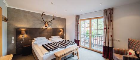 A bedroom with a large bed, a bench, a headboard with antlers, and a view of the outdoors through a window.