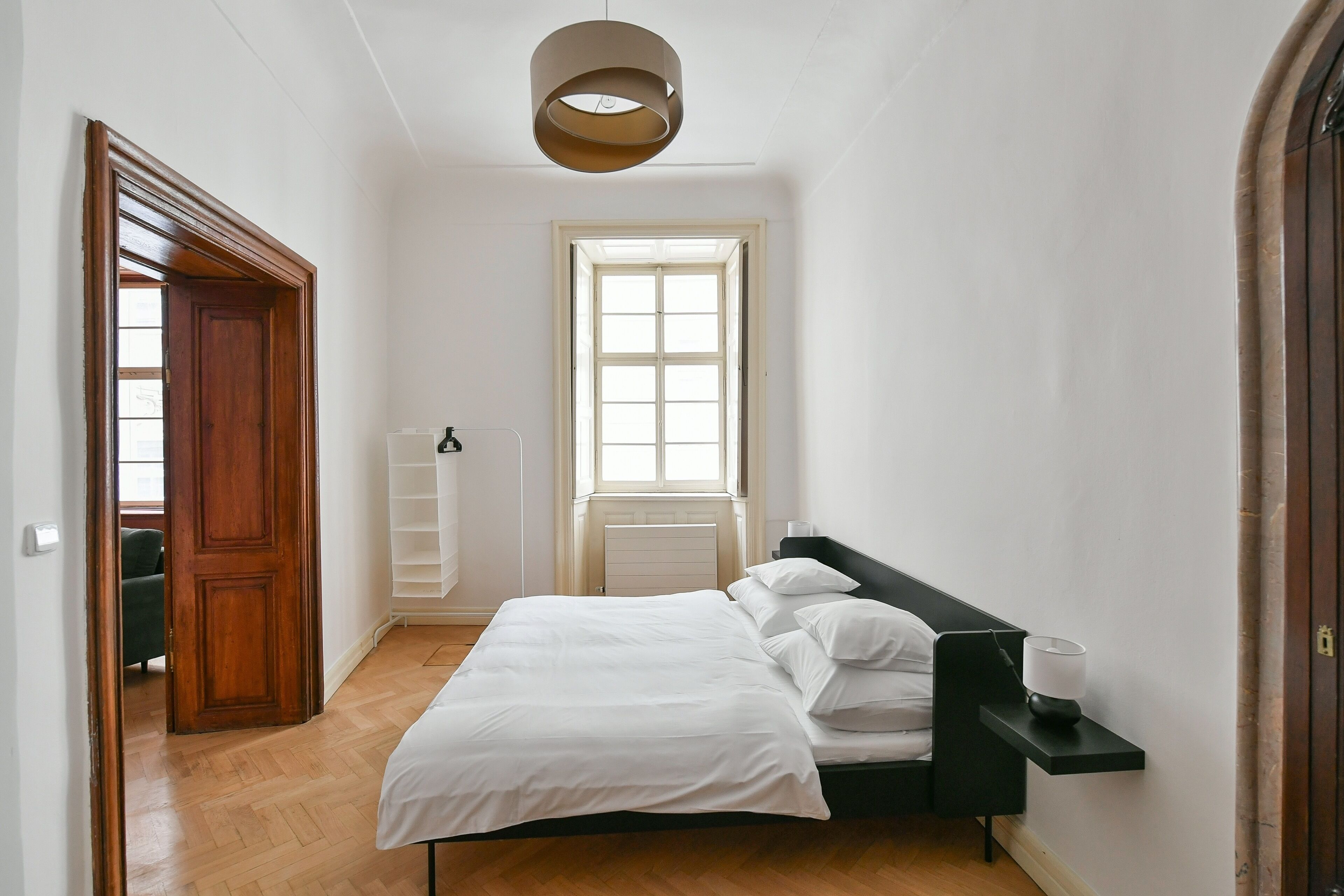 A bedroom with a bed, a bedside table, a window, and a radiator.
