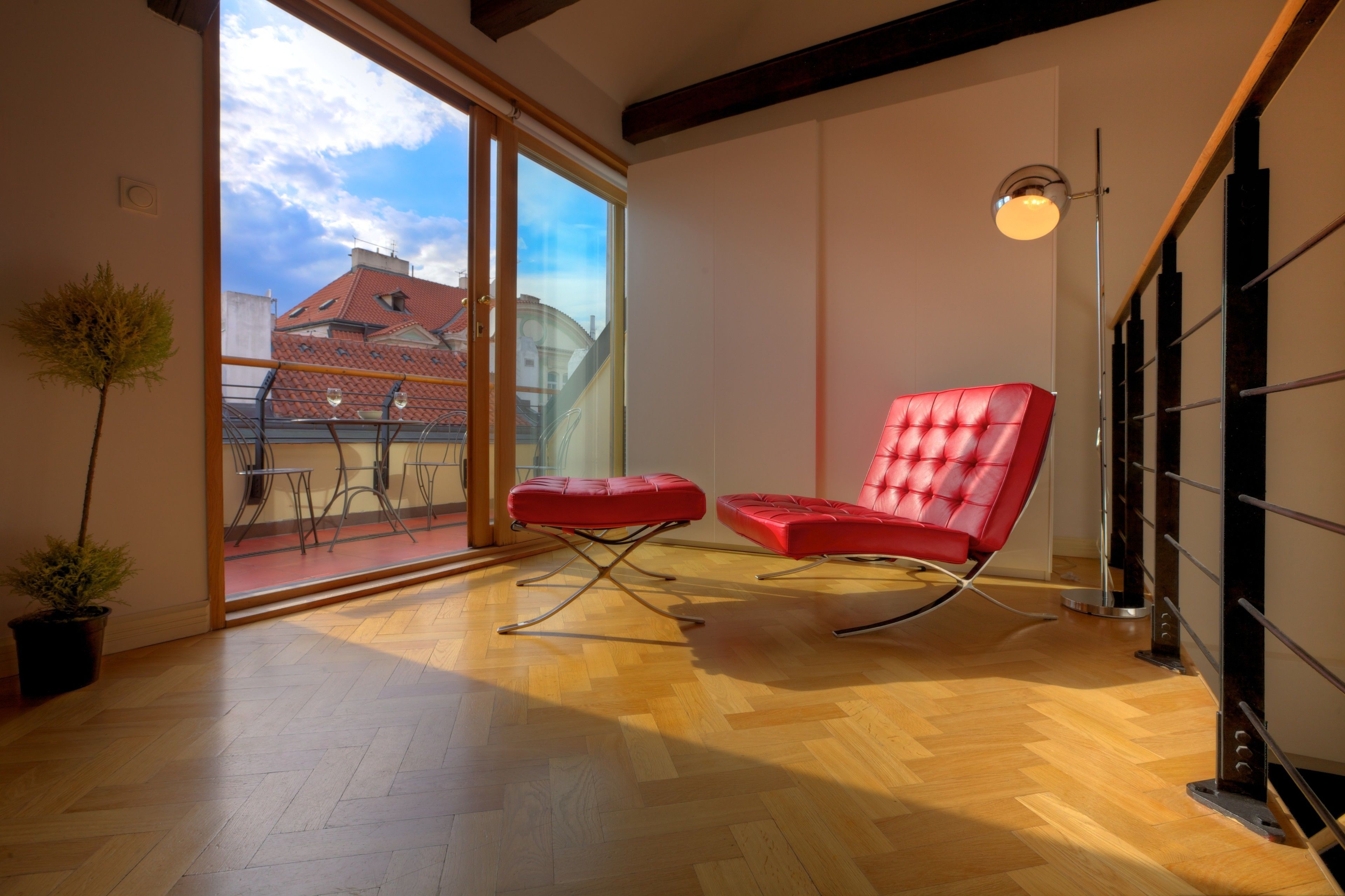Une chambre moderne avec un fauteuil en cuir rouge, une plante en pot et une grande fenêtre donnant sur les bâtiments environnants.