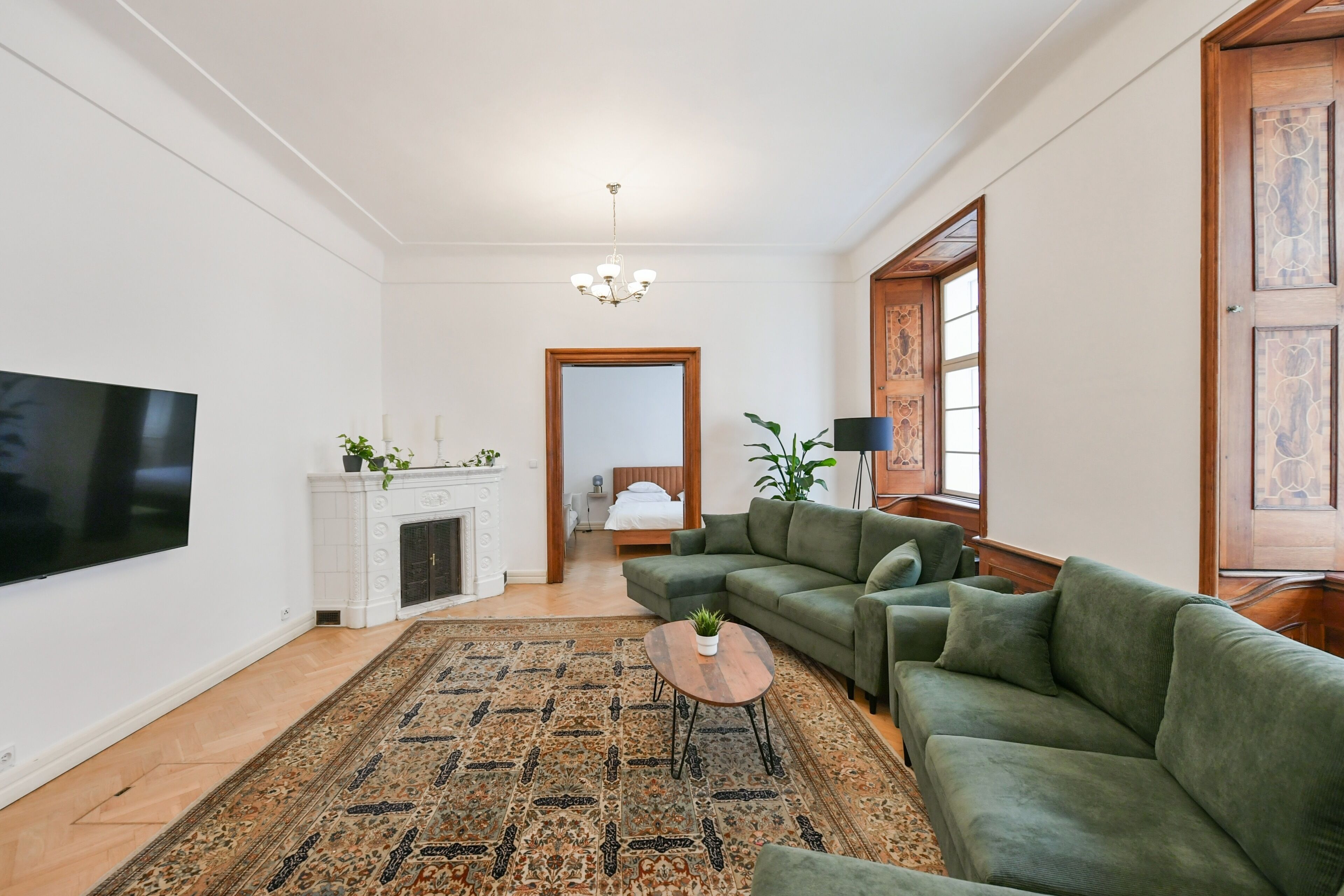 A living room with a green sofa, a flat-screen TV, a fireplace, and a patterned rug.