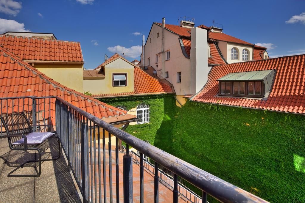 Un patio con césped verde y techos de tejas rojas, rodeado de edificios con balcones y una silla.