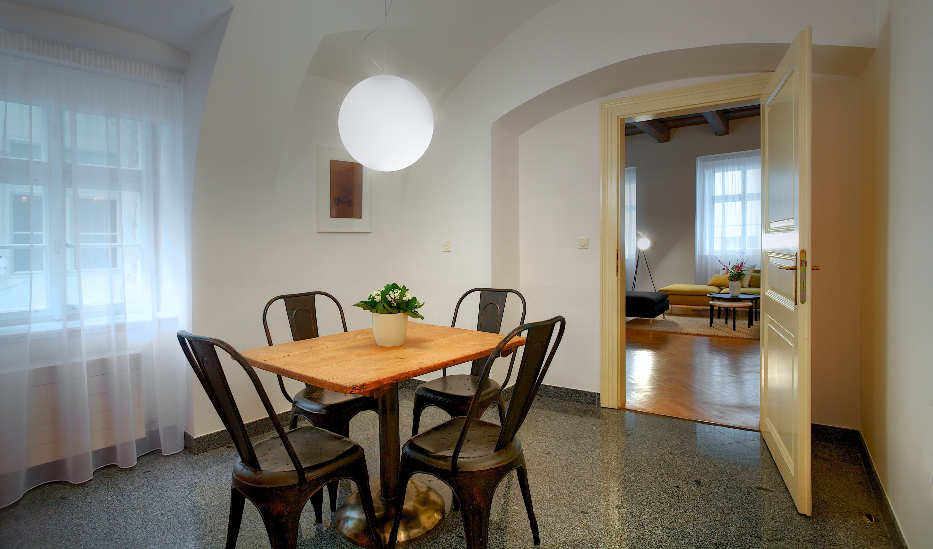 A dining area with a wooden table, four chairs, a potted plant, and a pendant light.