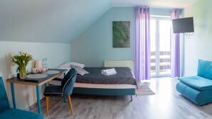 A bedroom with a bed, a desk with a chair, a blue sofa, a TV mounted on the wall, and a sliding door leading to a balcony. - Villa i Restauracja Tymotka (Lublin)