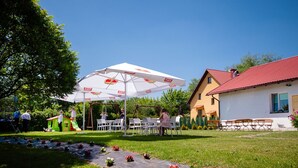 An outdoor seating area with white plastic chairs and a large white umbrella with red and white logos. - Villa i Restauracja Tymotka (Lublin)