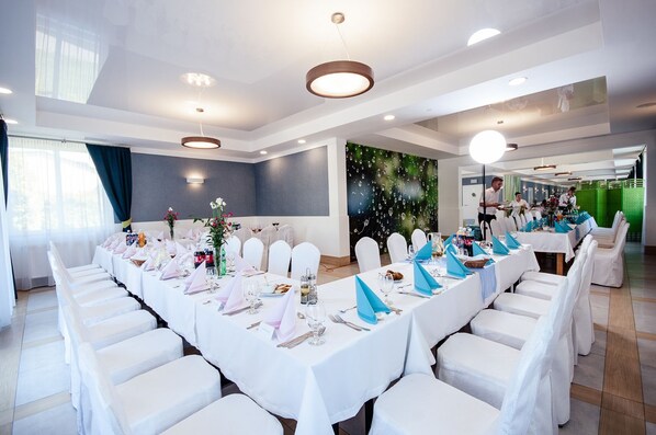 A banquet hall with long tables set for a formal event, white chairs, and a green wall with a pattern. - Villa i Restauracja Tymotka (Lublin)