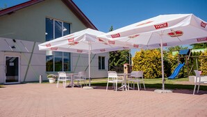 An outdoor seating area with white umbrellas and chairs in front of a building with a red roof. - Villa i Restauracja Tymotka (Lublin)