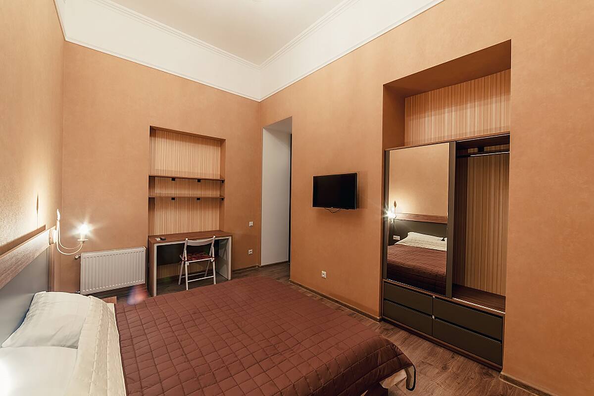 A hotel room with a bed, a desk, a chair, a TV, and a wardrobe.